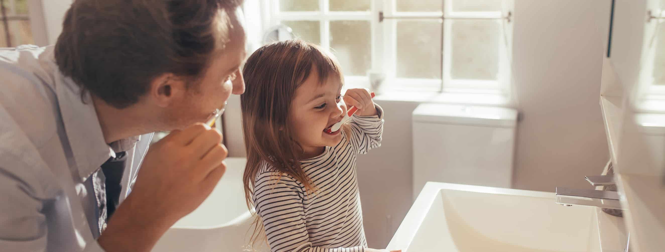 A young girl in Cincinnati  learning how to brush her teeth with her dad.