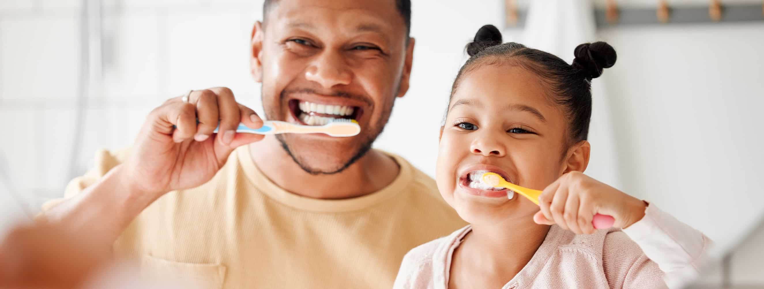 Father and Daughter looking in the mirror brushing thier teeth.